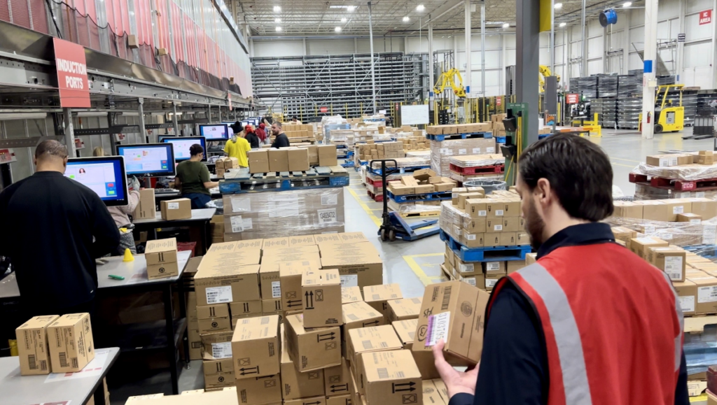 Warehouse workers managing inbound carton flow at automated induction ports with conveyor systems and WMS workstations